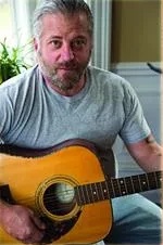 Stevie “C-Note” Cunningham smiling with an acoustic guitar