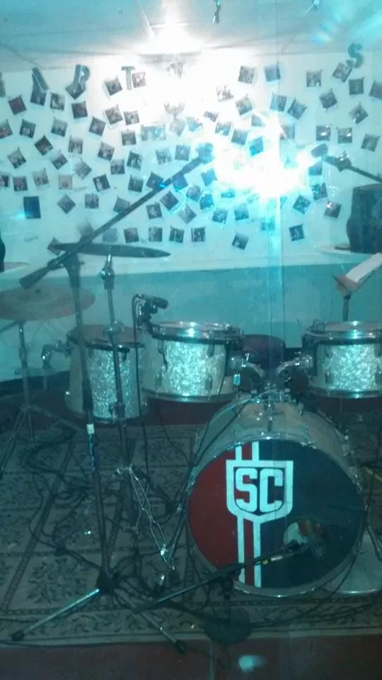 A drum kit in the studio in front of a wall of instant photos