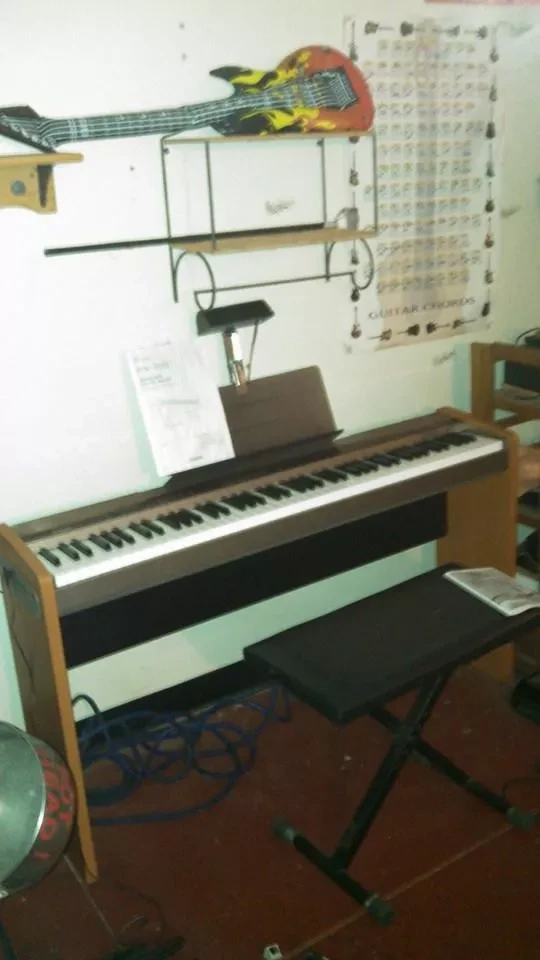 A digital piano and bench under a guitar chord chart